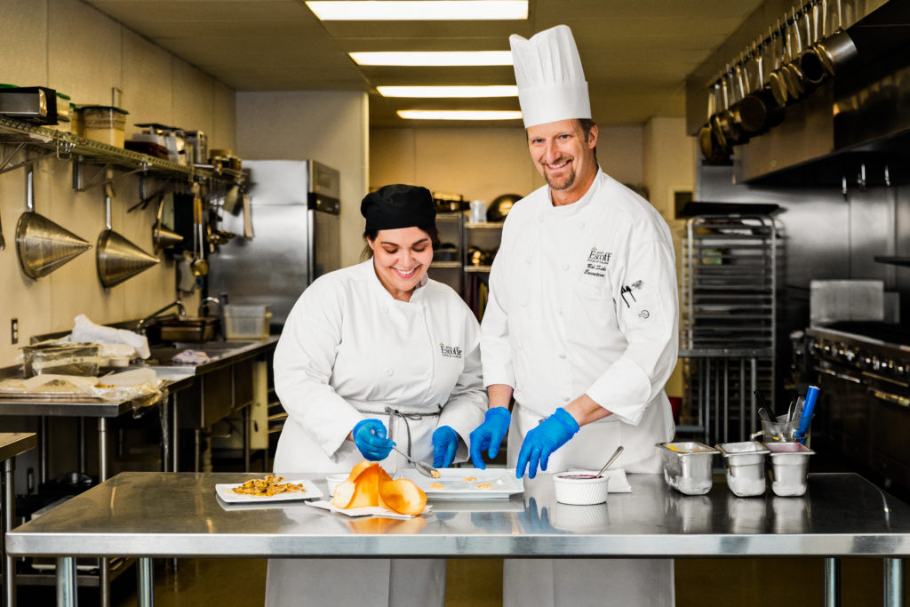 Male chef instructor Bob Scherner showing female student how to plate a dish