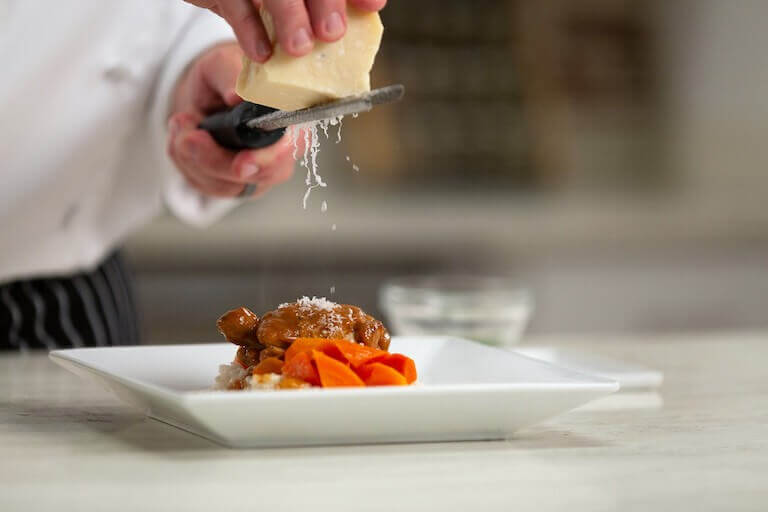 Chef grating cheese over a meat dish