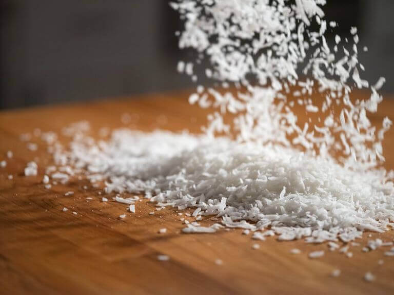 Dried coconut flakes being poured onto a wooden table