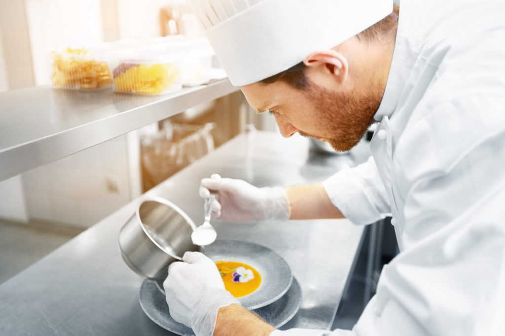 male chef cook serving and plating plate of soup with flower at restaurant kitchen