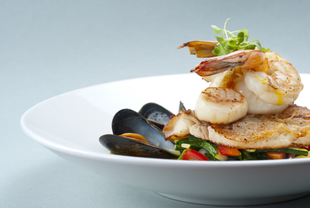 Seafood, shrimp, scallops and mussels on a white plate of vegetables