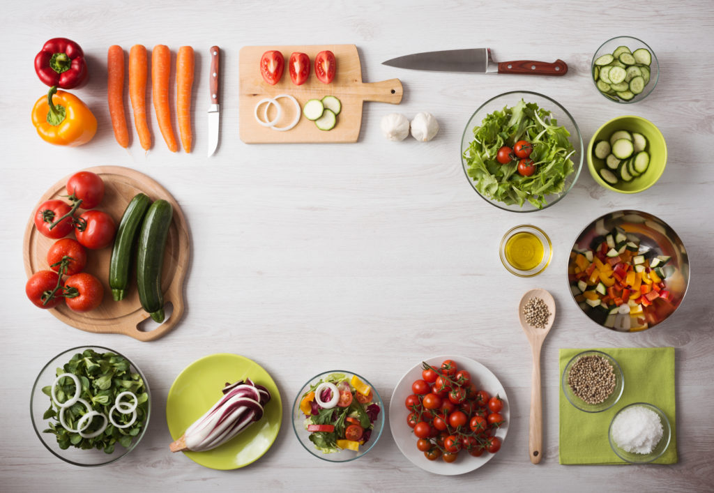Vegetables and knives and salad organized in a rectangle on a wooden table