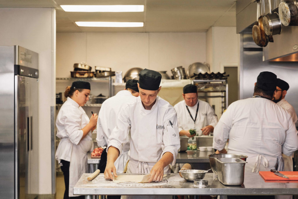 Male Escoffier culinary student rolling dough and flour in a kitchen