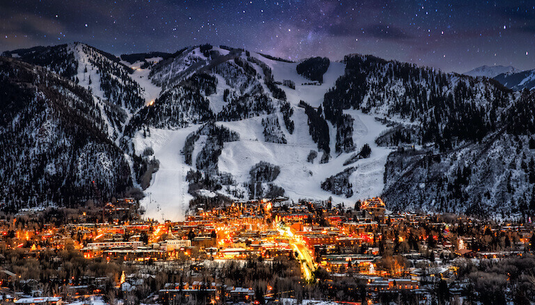 A distant view of Aspen at the foot of the Colorado Rockies beneath a starry night sky.