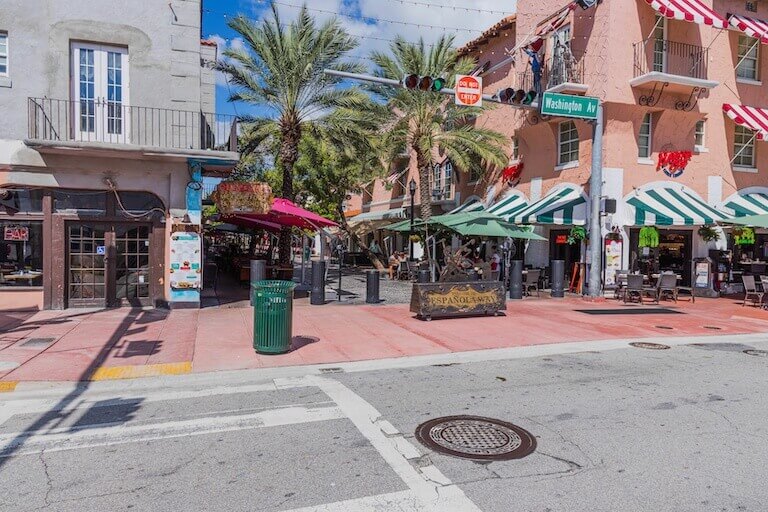 A street lined with restaurants in Florida, including palm trees and a deep blue sky.