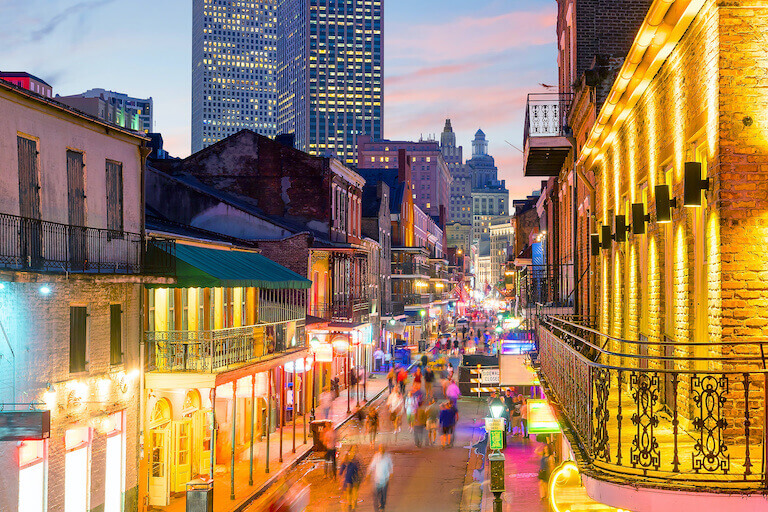 A sunset shot of the French Quarter in New Orleans with classic french architecture and a large group of people in the street.