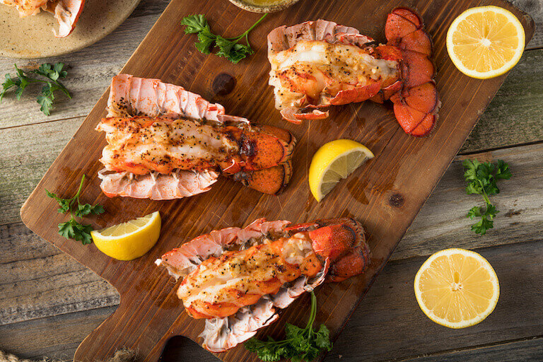 A trio of cooked lobsters, slathered in butter, sits on a wooden cutting board.