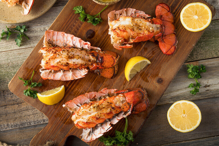 A trio of cooked lobsters, slathered in butter, sits on a wooden cutting board.
