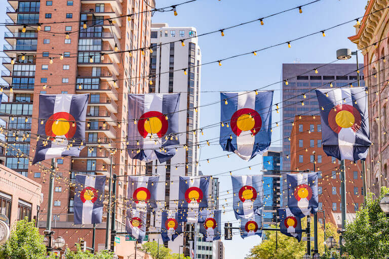 Shrink lights hang above a street in downtown Denver with numerous Colorado state flags hanging among them.