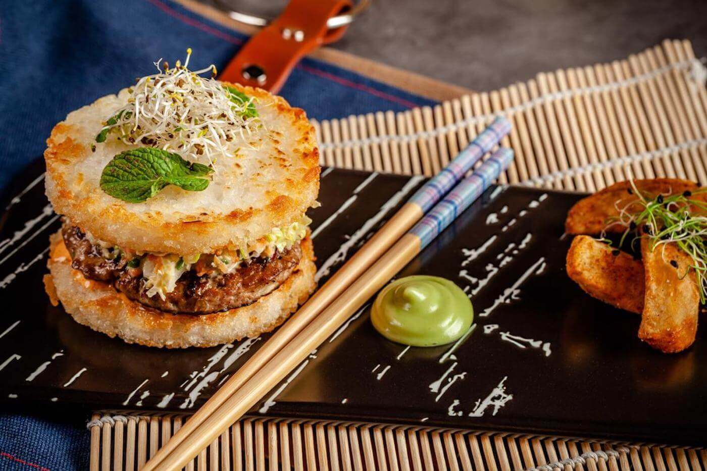 Burger with a rice bun sitting on a plate with chop sticks