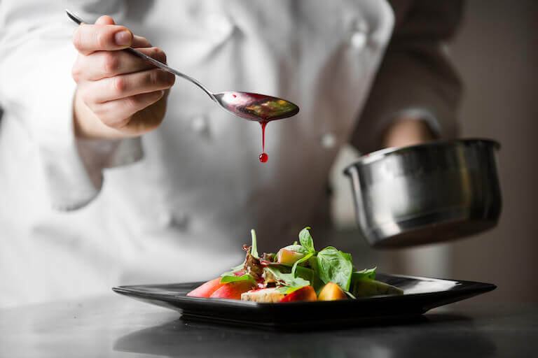 Chef using a spoon to pour sauce over a plate of food