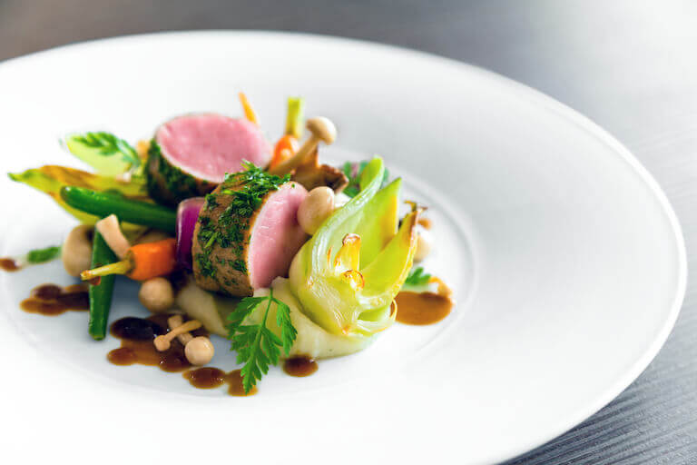 Fancy plated meat dish with vegetables on a white plate