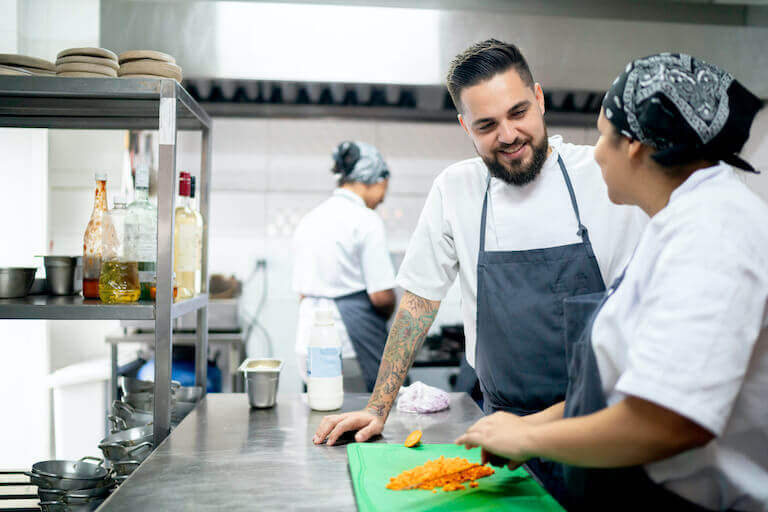 Two chefs talking in a kitchen while cutting carrots