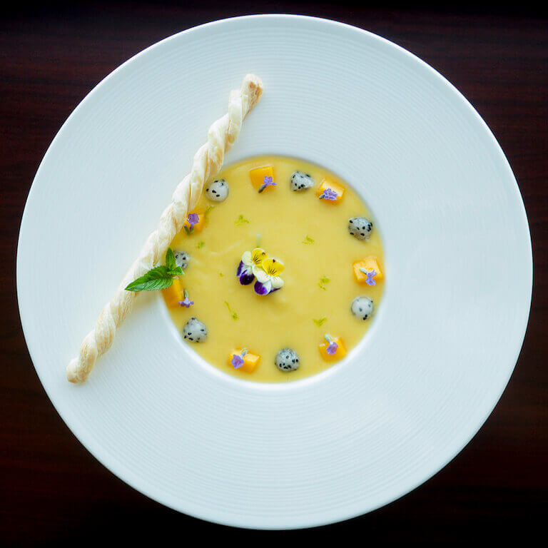 cold fruit soup garnished with flowers in a white bowl