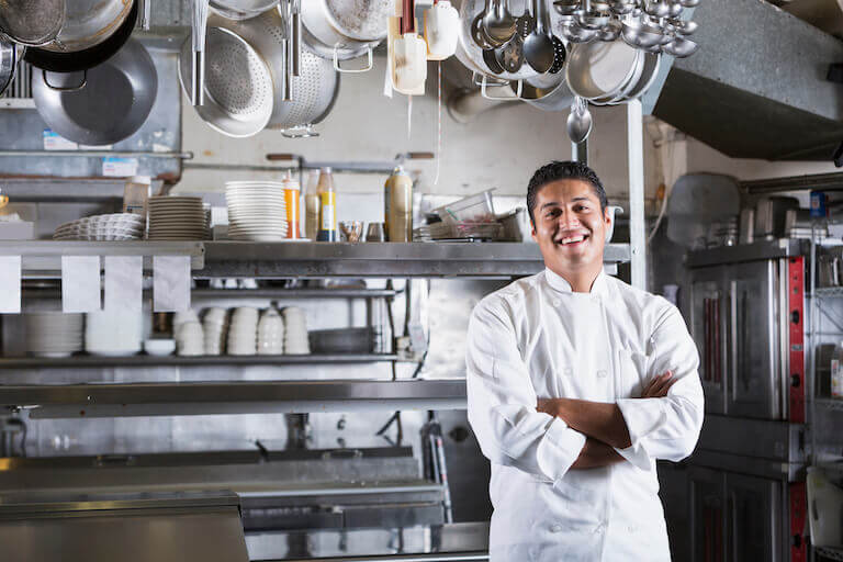 Chef standing with his arms crossed in a kitchen in front of pots and pans