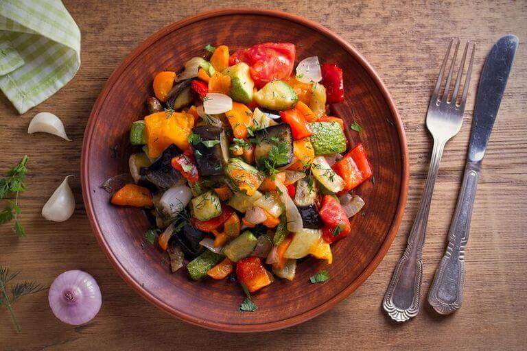 Overhead view of a bowl of vegetable stew with eggplant, pepper, tomato, zucchini, carrot, and onion.