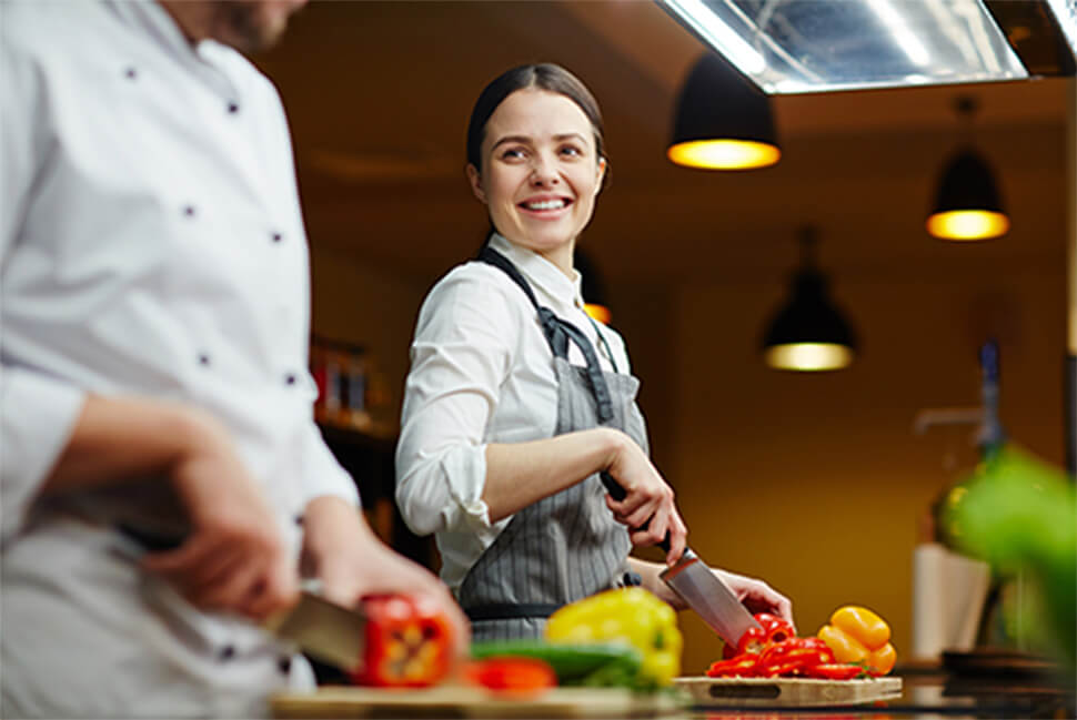 A chef smiles as they cut a pepper