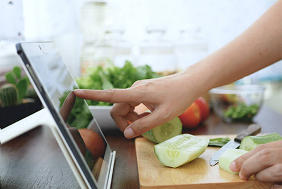 Online student using a tablet in the kitchen while they cut cucumbers