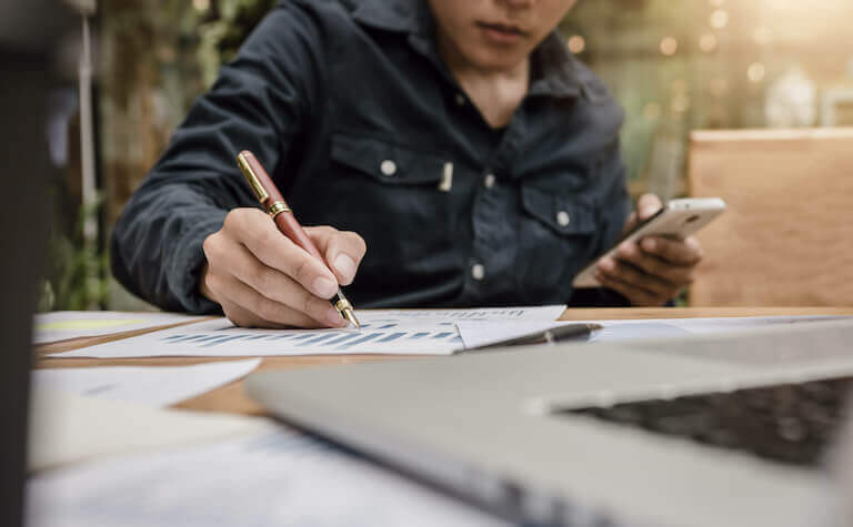 Businessman writing on paper graph and holding smartphone searching data