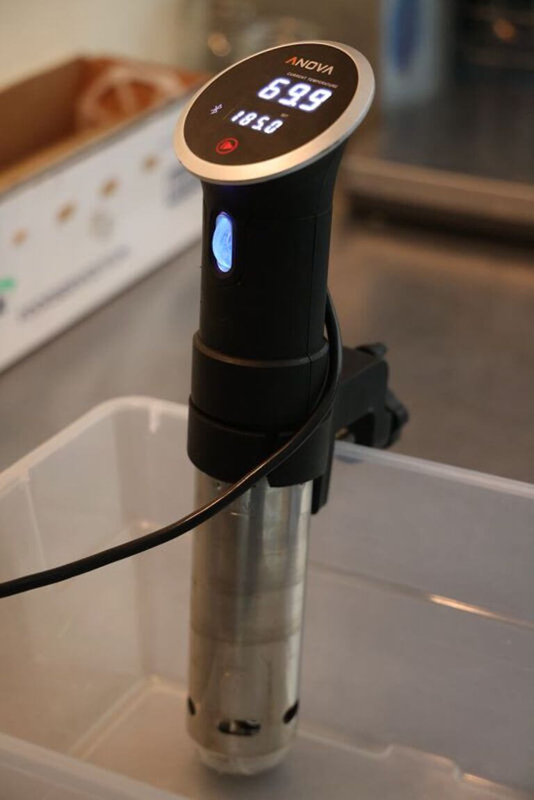 Sous vide cooker attached to a clear container showing a temperature of 69.9