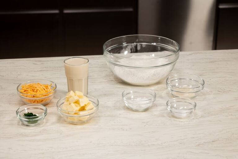 Cheese, flour, and other ingredients for biscuits in glass bowls