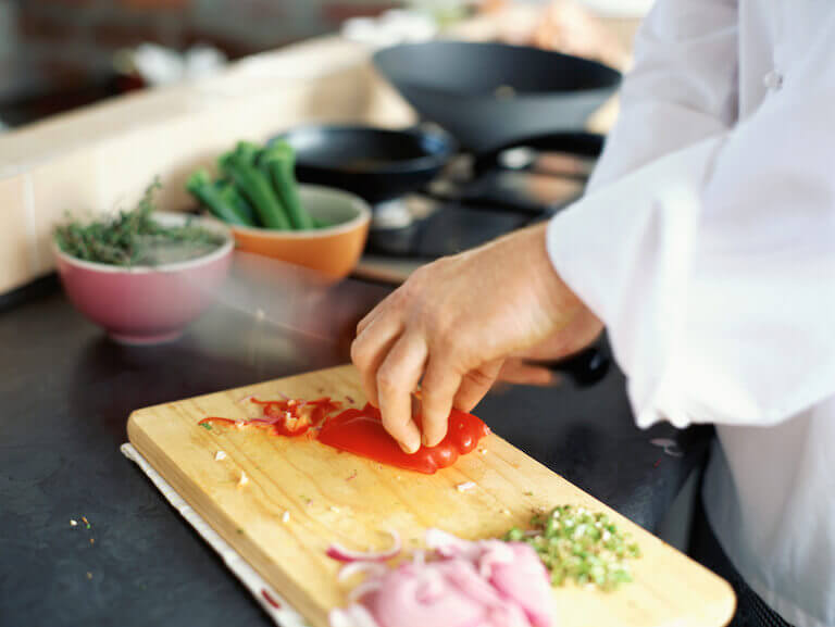 Chef chopping a red bell pepper and onions on a wooden cutting board