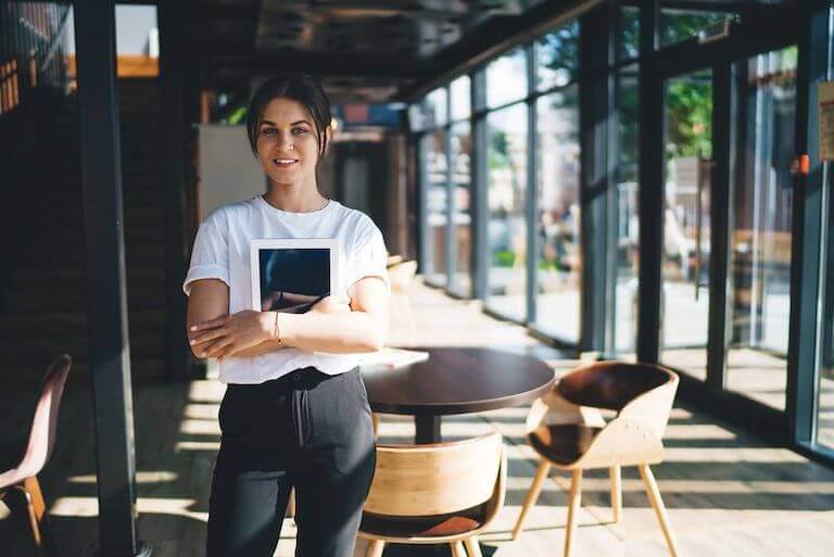 Restaurant employee wearing black and white standing in front of a table holding a tablet