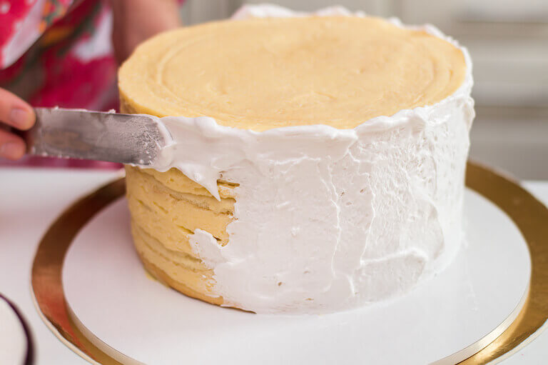 Cake decorator adding white frosting to a cake