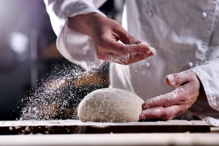 Close up photo of a baker sprinkling flour over dough