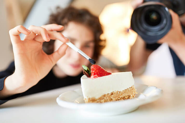 Food stylist holding a small brush over a strawberry on a slice of cheesecake