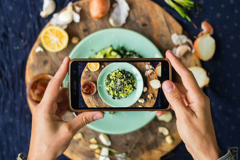 Hands holding a phone taking a photo of a plate with food