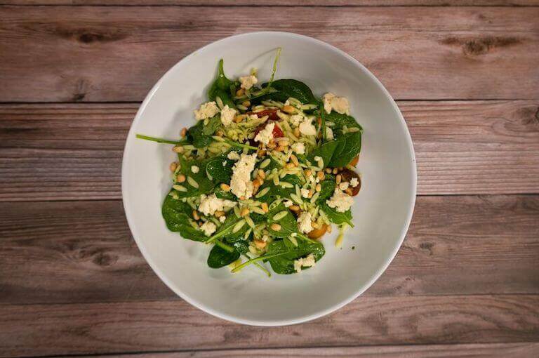 Orzo salad with spinach in a white bowl 