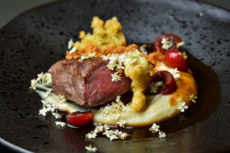 Venison Steak with Sweet potato and vegetables styled on a black plate