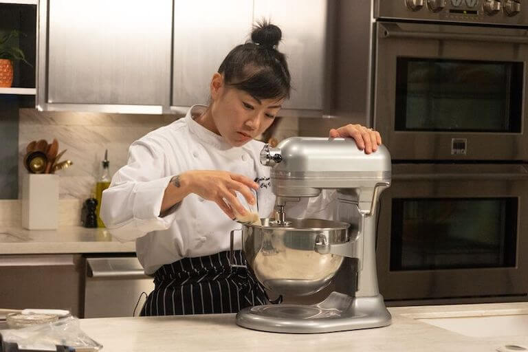 Chef pouring ingredients into a silver automatic mixer