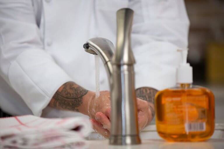 Close up of chef washing hands with orange soap bottle next to sink