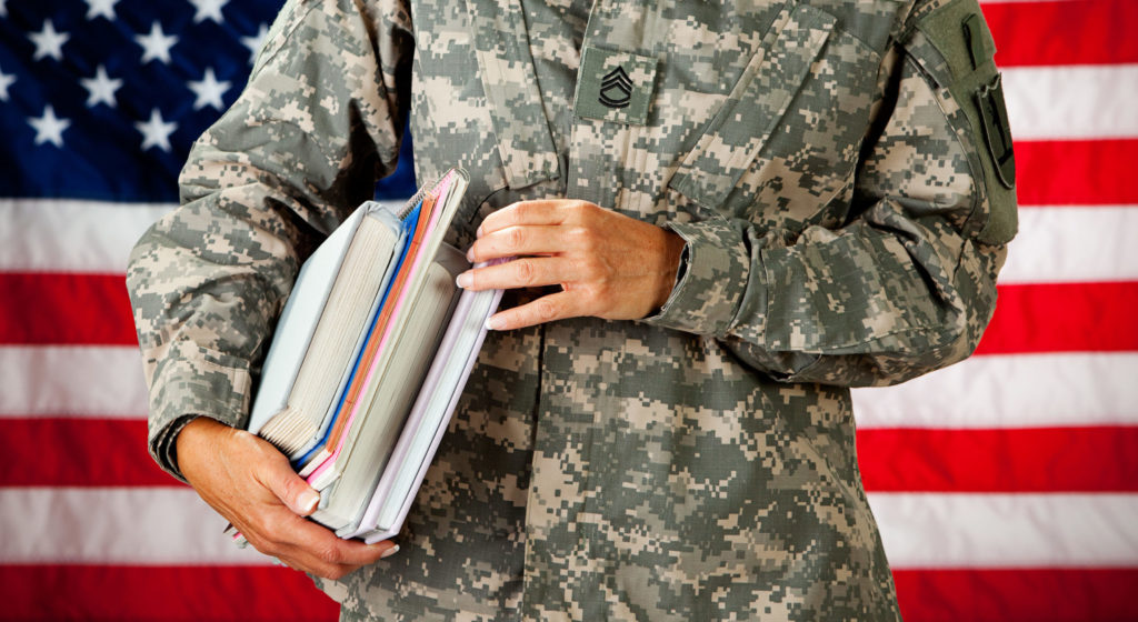Uniformed soldier standing in front of american flag with books