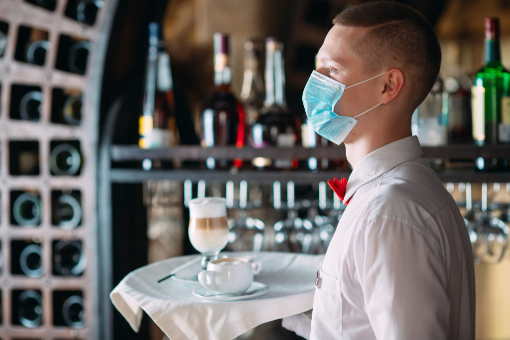 Waiter in a medical mask serves Latte coffee