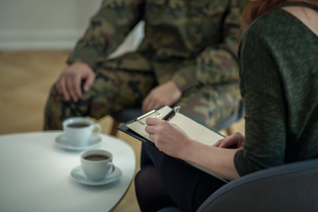 psychologist writing down notes while talking to her patient from army
