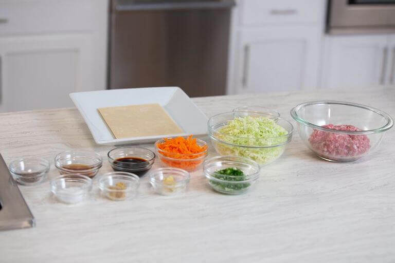 Carrots and other egg roll ingredients separated into small glass bowls