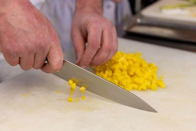 Chef chopping yellow vegetable on a cutting board