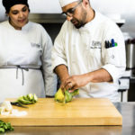 Male chef instructor showing female culinary student how to chop vegetables