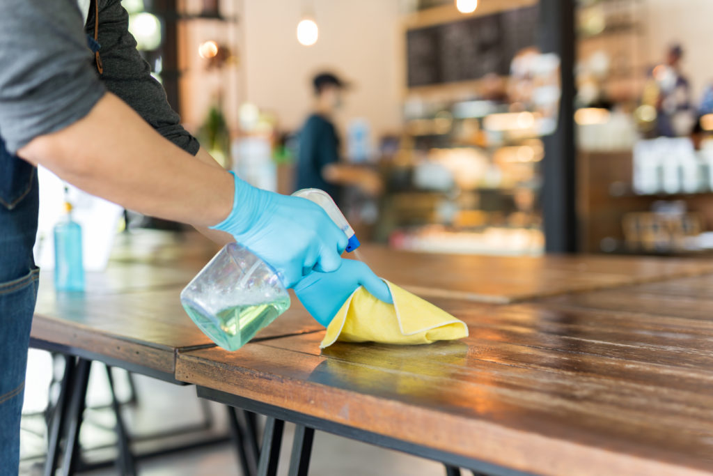 Waiter cleaning table with disinfectant spray and microfiber cloth in cafe