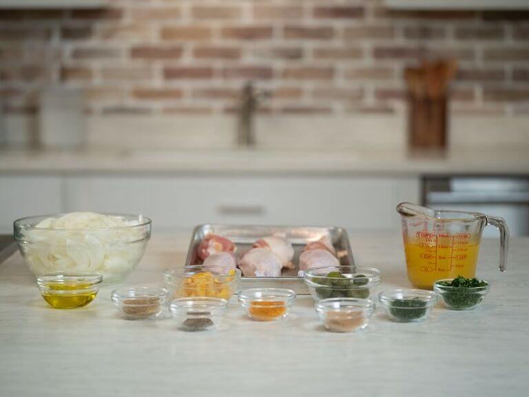 Raw chicken, onions, and other ingredients for tagine seperated into glass bowls on a counter