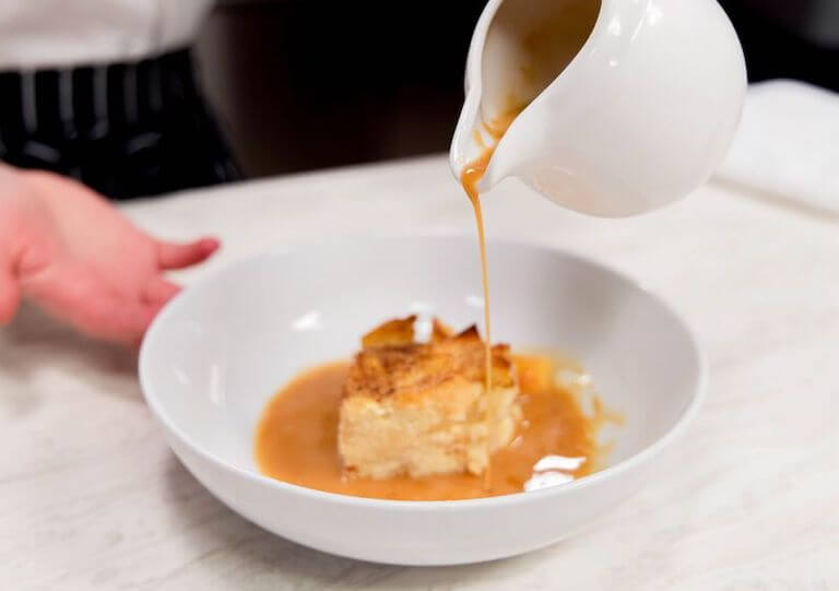 Chef pouring sauce on bread pudding in a white bowl