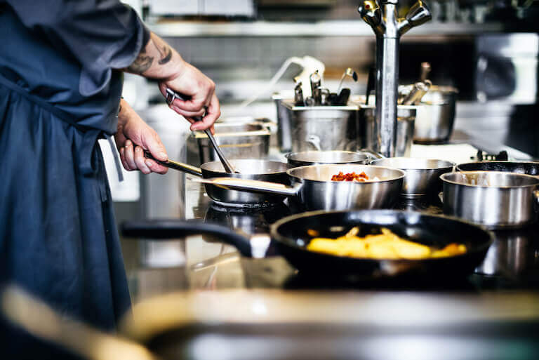 Chef stirring food in a pot on a stove with multiple pots and pans