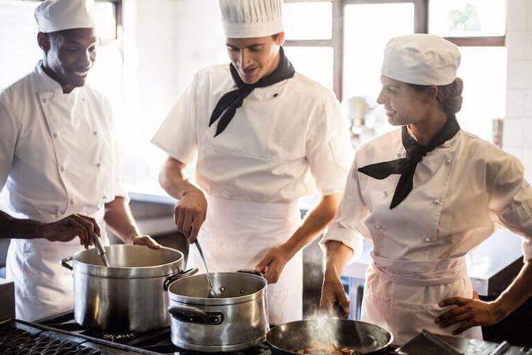Chefs wearing neckties stirring metal pots in a kitchen