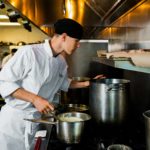 Escoffier culinary student checking a pot in a professional kitchen