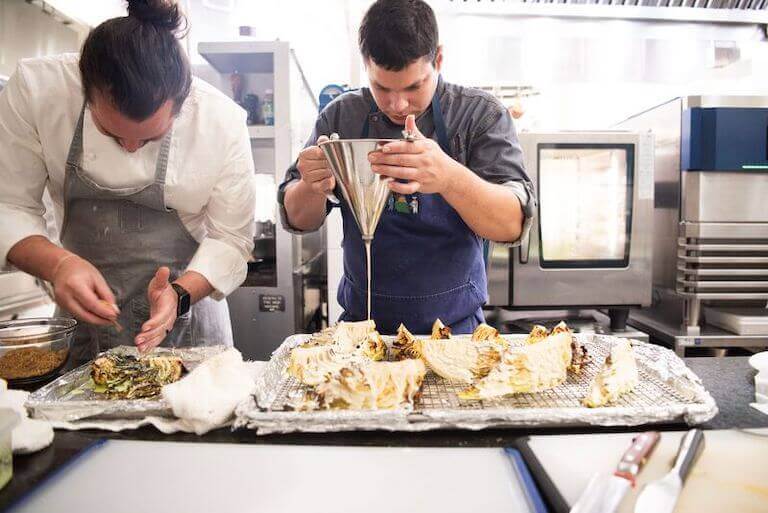 Escoffier student pouring sauce in a kitchen at an immersive farm-to-table event