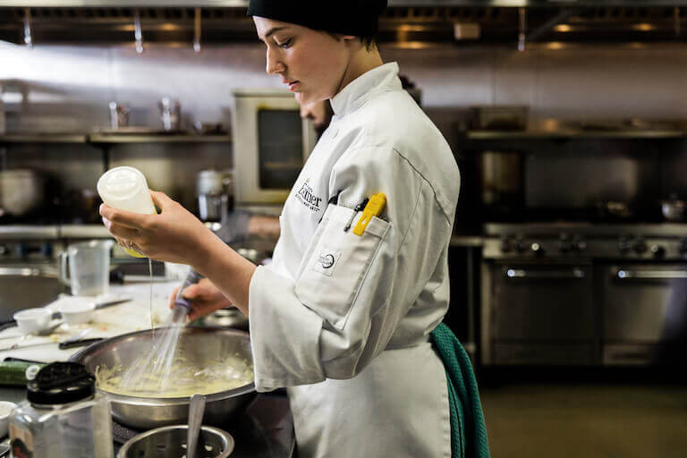 Escoffier student whisking a bowl as she adds ingredients