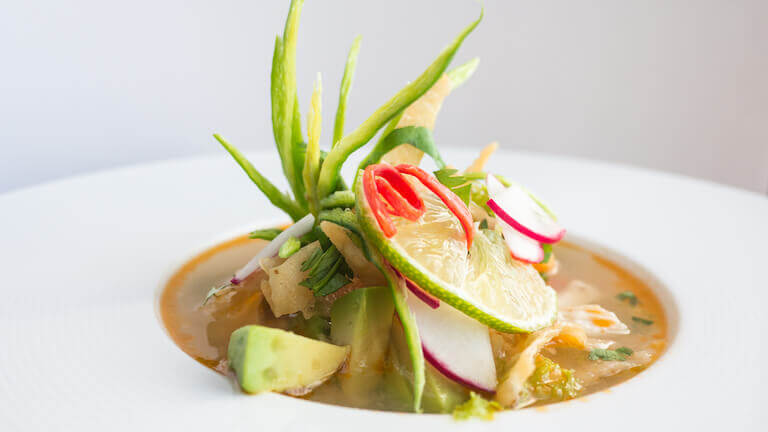 Soup in a white bowl garnished with avocado and other vegetables